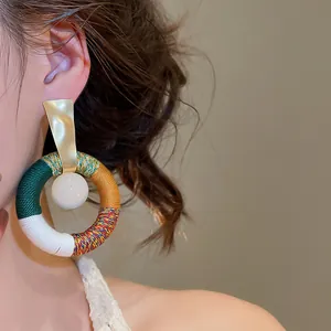 Detailaufnahme eines runden Ethno-Ohrrings mit buntem Baumwollseil und weißer Harzperle