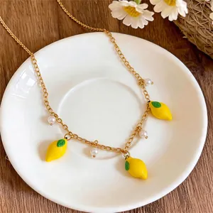 Fresh gold chain necklace featuring yellow lemon pendants and white pearls on white saucer
