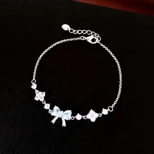 Elegant silver bracelet with light blue zircon bow and flower pendants on black background.