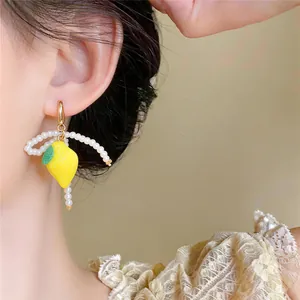 Close-up of fresh lemon pendant earrings with delicate white pearl strands decoration