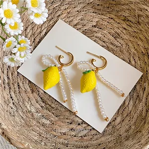 Macro detail of fresh yellow lemon earrings featuring elegant pearl beads and gold hoops
