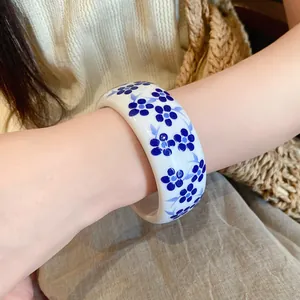 Detailed close-up of a retro blue and white floral resin bangle worn on a wrist