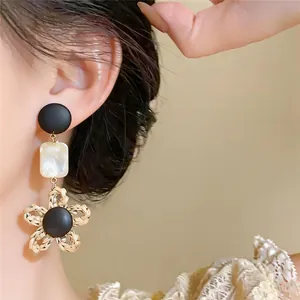 Détail rapproché de boucles d'oreilles fleur vintage avec texture tissée et accents de marbre sur modèle