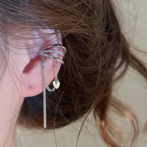 Detail eines silbernen mehrlagigen Ohrclips mit Herzanhänger und Ketten an einem Ohr