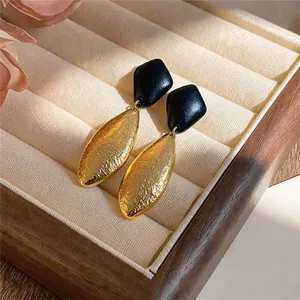 Makroansicht der faltigen Goldtextur und der schwarzen geometrischen Stecker dieser Ohrringe.