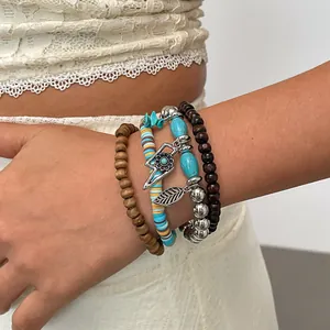 Detailweergave van gelaagde etnische armbanden met houten kralen en bedeltjes om de pols.