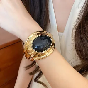 Nahaufnahme eines goldfarbenen Manschettenarmbands mit großem schwarzem ovalem Harz