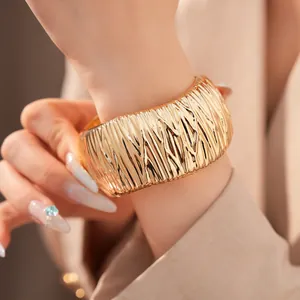 Detailansicht der plissierten goldenen Metallstruktur eines klobigen Armreif-Armbands.