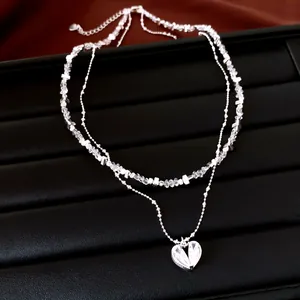 Gros plan d'un collier double rang argenté avec pendentif cœur et perles de cristal.