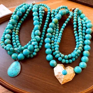 Elegante meerlaagse turquoise kralenketting met grote gouden hart- en druppelvormige hangers.