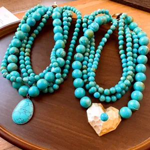 Detail van de gelaagde turquoise kralenketting met een grote goudkleurige harthanger