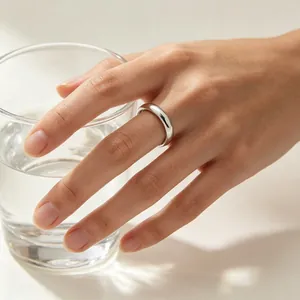 Detail view of a 4mm minimalist stainless steel plain band ring on a hand holding a glass