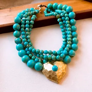 Detail van meerlaagse turquoise kralenketting met goudkleurige gehamerde hart hanger