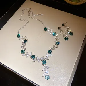 Gedetailleerd overzicht van groene strass bloem en blad ketting en oorbellen set in doos