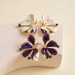 Close-up of elegant purple and white enamel flower earrings with sparkling blue crystals.