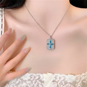 Detailopname van een zilveren ketting met een sprankelende blauwe kruishanger op een model