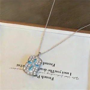 Detailopname van een zilveren ketting met rechthoekige hanger en blauw zirkoonkruis