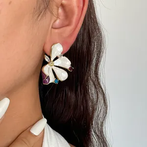 Close-up of elegant flower stud earrings featuring white enamel petals and colorful crystals