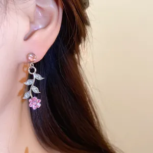 Close-up van elegante bloem- en bladhangers met roze strass-steentjes getoond op het oor
