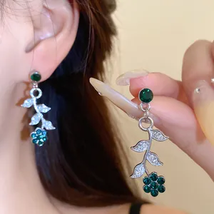 Detail van zilveren oorbellen met bladeren en bloemen en groene glanzende strass