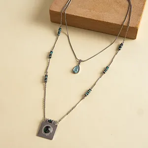 Vue détaillée d'un collier en acier inoxydable argenté avec pendentifs goutte et carré.