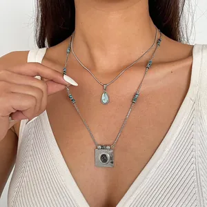 Détail de colliers superposés en acier inoxydable avec pendentifs goutte en résine