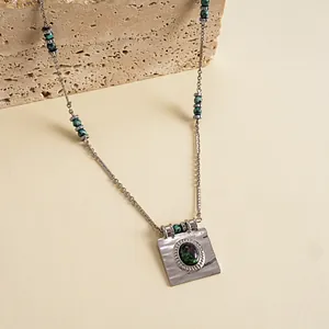 Gros plan d'un collier en acier inoxydable avec un pendentif carré en rubis zoisite sur pierre.