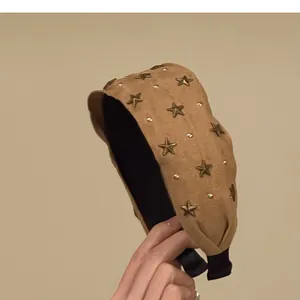Detailopname van een beige suède haarband met bronzen sterren en zwart elastiek.