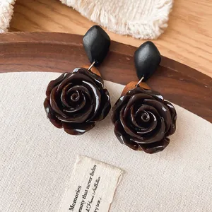 Close-up of vintage dark brown resin rose earrings with black geometric studs
