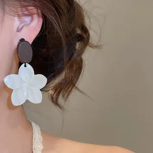 Close-up of vintage floral earring with white flower petals and brown oval top on model ear.