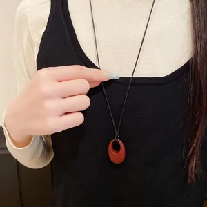 Detailansicht einer minimalistischen Halskette mit rotem ovalem Anhänger und schwarzer Kordel.