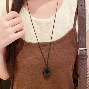 Detailansicht einer minimalistischen Kette mit schwarzem ovalem Anhänger und Lederband