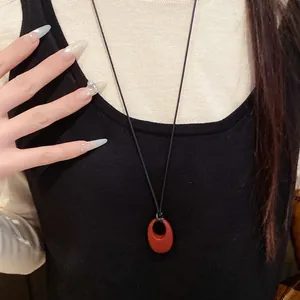 Detailansicht einer minimalistischen Halskette mit einem roten ovalen Anhänger aus Leder.
