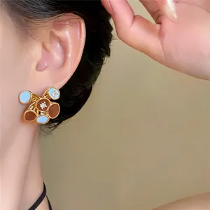 Close-up of 18k gold plated earrings with blue and brown oil drip polka dot design