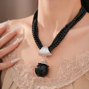 Detailansicht einer dreilagigen schwarzen Perlenkette mit einem großen Kugelanhänger.