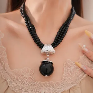 Exquisites Detail einer dreilagigen schwarzen Acryl-Perlenkette mit markantem Kugelanhänger