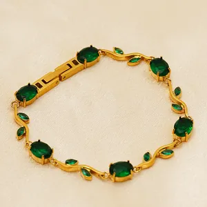 Détail d'un bracelet doré avec des zircons ovales vert émeraude et des pierres en forme de feuille.
