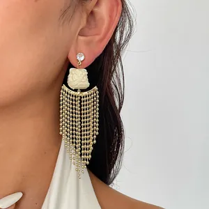 Boucles d'oreilles tête de lion en résine blanche avec longues franges dorées portées.