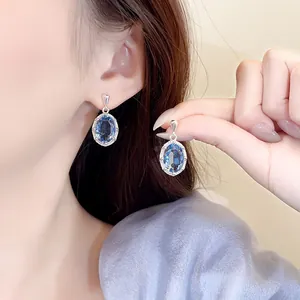 Detailweergave van luxe ovale blauwe zirkoon oorbellen met een sprankelende halo.