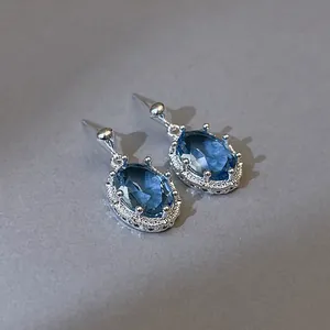 Detail van elegante ovale blauwe zirkoon oorknopjes met zilverkleurige halo-zetting