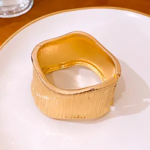 Primer plano de brazalete dorado con textura vertical y cierre de hebilla elegante.