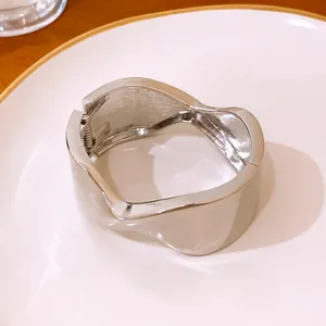 Vista detallada de un brazalete plateado retorcido con cierre de bisagra lateral minimalista