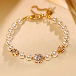 Détail en gros plan d'un bracelet doré avec des zircons carrés et des perles blanches.