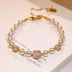 Vue macro d'un bracelet doré avec des perles blanches et des accents de zircon carrés.