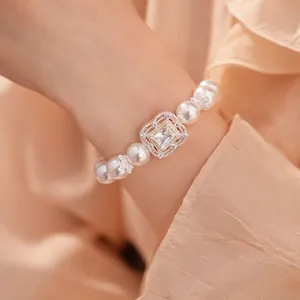 Elegantes Perlenarmband mit quadratischem Zirkonia-Blumenanhänger am Handgelenk einer Frau