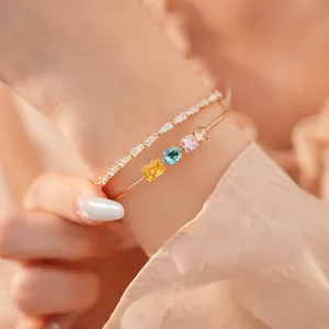 Nahaufnahme eines 18k vergoldeten Doppelarmbandes mit bunten Zirkonsteinen am Handgelenk.