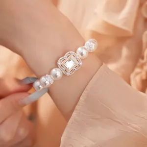 Detailansicht eines eleganten Perlenarmbands mit quadratischem Zirkon-Herzstück am Handgelenk