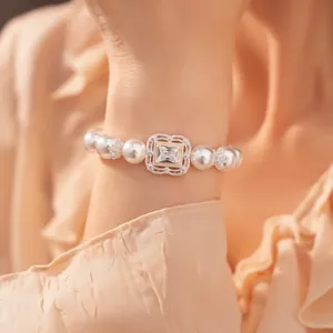 Makro-Detail eines eleganten weißen Perlenarmbands mit quadratischer Zirkonia-Blüte am Handgelenk