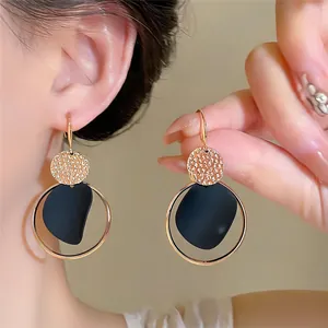 Primer plano de pendientes de aro dorados con disco texturizado y placa negra mate