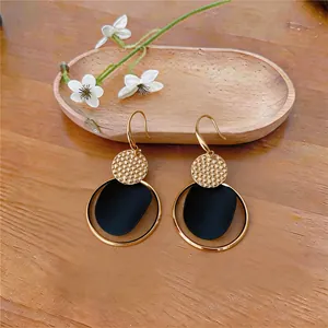 Detalle de pendientes de aro dorados con pétalo negro y disco dorado texturizado.